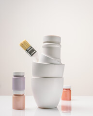 Vertical composition with paint cans, jars and a brush on a light background with copy space. Mockup for paints, lacquers. Artist's workplace, preparation for decorative, creative and artistic works