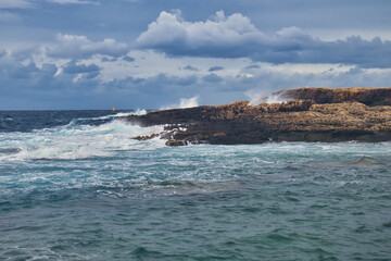 Water splashing in and on the rocks on a beach at Qawra, Malta on a cloudy day.