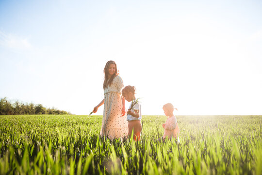 A mother with two daughters is walking in a green field. Hugs and feelings.