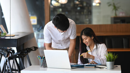 Two young designer working with laptop computer and discussing over new business project in modern office.