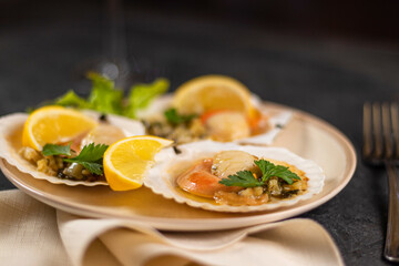 Baked scallops with caviar in a plate against the background. Scallops with lemon on a black background with a napkin and a fork.