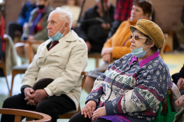Elderly people in medical masks sit on chairs.