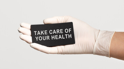 Closeup of the hand in a white sterile glove holding a card with text - take care of your health