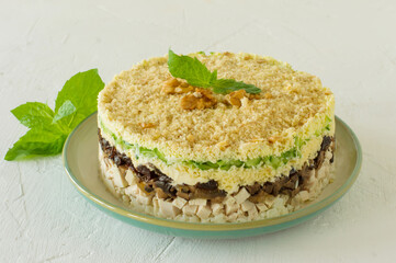 Layered salad with chicken, mushrooms, prunes, eggs, cucumbers and cheese served on a plate on white background