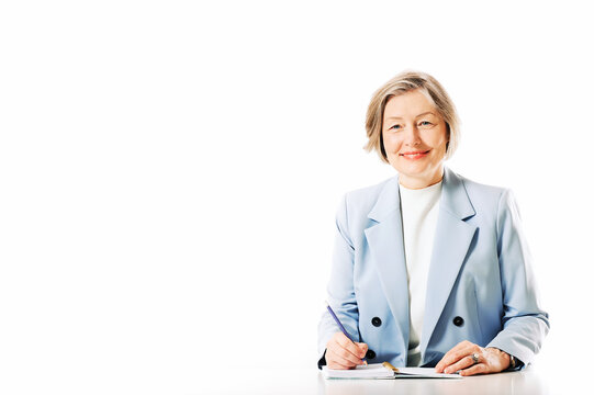 Studio portrait of middle age woman posing on white background, sitting at the desk and taking notes