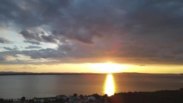 Reveal shot from colourful clouds to dipping sun in the Adriatic Sea. Romantic sunset Vrsi Mulo, Croatia