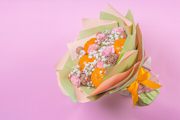 A bouquet of fruits in hand on a pink background. Juicy tangerines with greta nuts and decorated with flowers on a pink background. The concept of a useful gift, congratulations on the holiday.