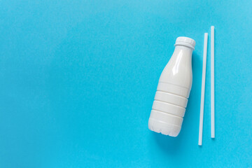 Milk bottle with straws on blue background, space for text