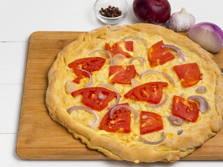 Homemade vegetarian pizza with tomatoes and onions on a wooden board on a white wooden background. The concept of healthy food.