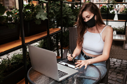 Young Woman Wearing Protective Face Mask Working on Laptop and Drawing Tablet While Sitting in Cafe Outdoors, Freelance Concept