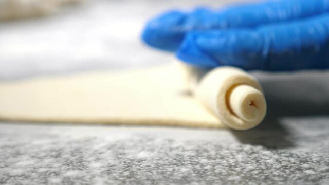 Female hands in gloves rolling a dought sheet to shape a croissant at a bakery plant 