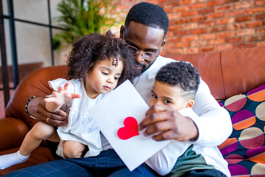 two children afro american baby giving to dad a Valentine's Day picture in living room
