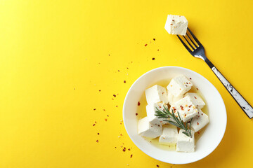 Bowl and fork with feta cheese on yellow background