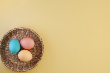 Minimalistic Easter composition with colorful Easter eggs in a wicker basket on a yellow trendy background with place for text, flat lay. Easter concept, Easter eggs painted in pastel colors
