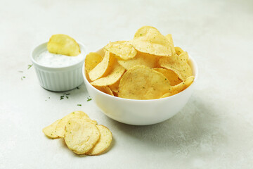 Tasty potato chips and sauce on white textured background