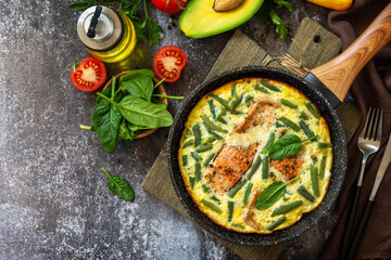 Breakfast or lunch snack concept. Rustic omelet (omelette, Scrambled)  with salmon fillet and green beans in a frying pan on a stone background. Top view, flat lay. Copy space.