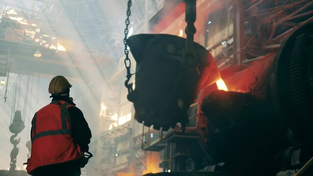 Metallurgical factory concept. Steel worker is observing melted metal pouring from the tank