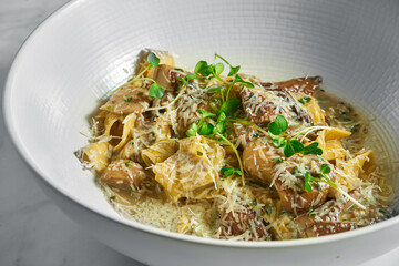 Pappardelle pasta with white forest mushrooms, mushroom sauce, grated parmesan and microgrine in a white bowl on a white marble background