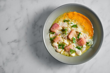 Peruvian cuisine dish - seabass ceviche with grapefruit and yellow sauce, served in a grey plate on a marble background. Restaurant seafood.
