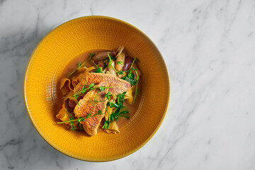 Pappardelle pasta with fried red mullet, barbule and microgrine in a yellow bright plate on a marble white background