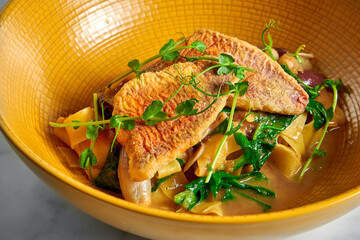 Pappardelle pasta with fried red mullet, barbule and microgrine in a yellow bright plate on a marble white background
