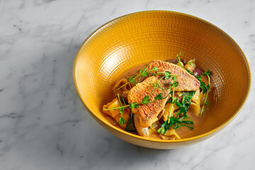 Pappardelle pasta with fried red mullet, barbule and microgrine in a yellow bright plate on a marble white background