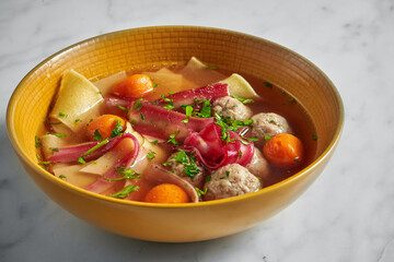Chicken soup with noodles, yolks, and meatballs on a marble background