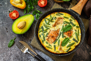 Breakfast or lunch snack concept. Rustic omelet (omelette, Scrambled)  with salmon fillet and green beans in a frying pan on a stone background.