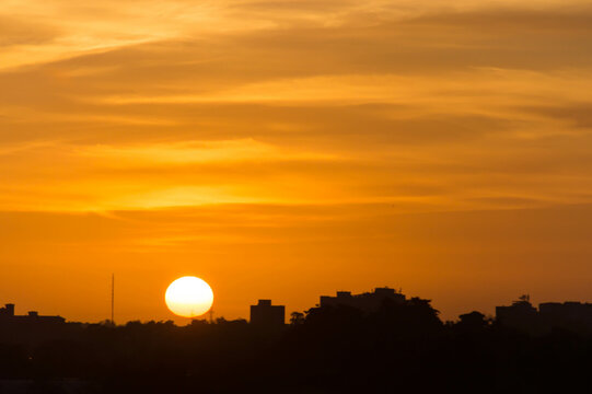 Silhouette of buildings in an urban area against a big round sun background at sunset