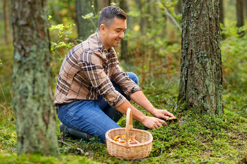picking season and leisure people concept - happy smiling middle aged man with wicker basket and mushrooms in autumn forest