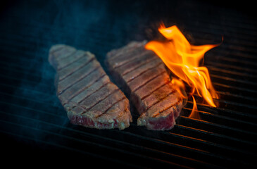 Two pieces of Striploin beef tips on getting grilled on a barbeque grill.GRILLING