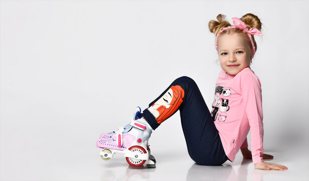 cute blonde girl in a pink sweater with a print and legends sits on the floor in roller skates. studio shot