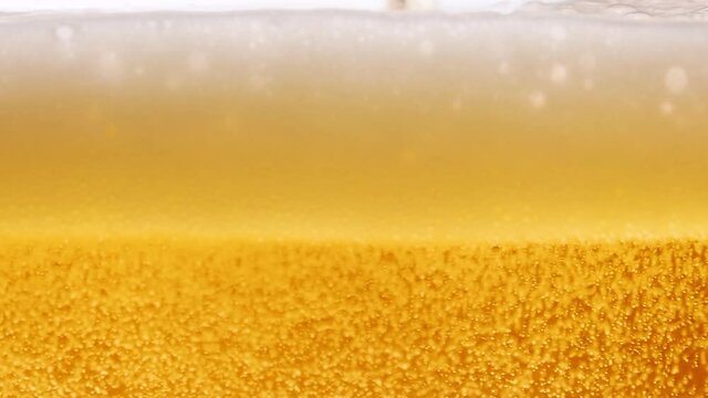 Light beer macro in glass. A thin trickle of golden liquid pours into the glass, creating many bubbles, waves and foam. Freshly brewed alcoholic beverage beer close up. Slow motion.