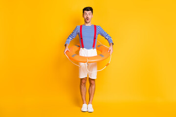 Full length photo of amazed brunette man hold lifeguard circle wear summer sailor outfit isolated on yellow color background