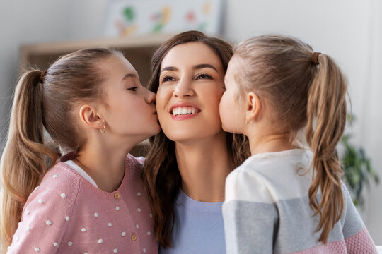 people, family and love concept - two daughters kissing happy mother at home