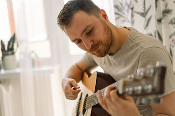 Man plays an acoustic guitar in a room at home. Hobby a musician.