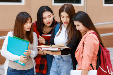 Group of four college student girls holding books standing and reading together. Learning and...