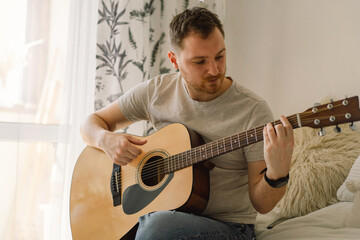 Man plays an acoustic guitar in a room at home. Hobby a musician.