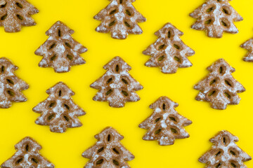 Christmas tree cookies on yellow background. New Year's food. Festive baked goods. Gingerbread on the table. Icing sugar sweetness taste season. Pattern