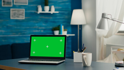 Laptop computer with mock up green screen chroma key display standing on table in living room. PC with isolated display in home office studio with nobody in it