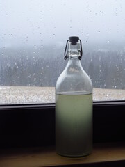 Szklana butelka z alkoholem przy oknie na parapecie, widok na zimowy pejzaż 