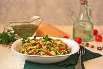 Italian food-pasta fettuccine with pesto, cherry tomatoes, walnuts and Parmesan cheese on a white plate on a concrete background. Selective focus.