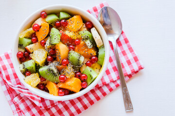 Bowl of healthy fresh fruit salad on white table. The view from the top. Healthy vegan lunch.