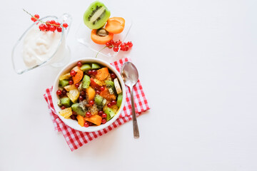 Bowl of healthy fresh fruit salad on white table. The view from the top. Healthy vegan lunch.