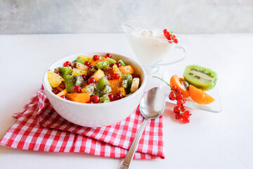 Bowl of healthy fresh fruit salad on white table. The view from the top. Healthy vegan lunch.
