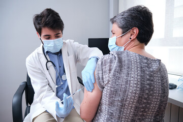 Doctor vaccinating mature woman patient in clinic. Nurse holding syringe before inject Covid-19 or...