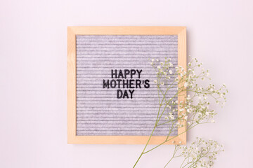 Happy Mothers day. Letter board and white gypsophila flower on a gray background. Festive layout.
