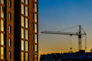 Big crane silhouette and many workers building new construction under a beautiful colorful sunset sky.Tall building under construction with scaffolds,Construction Site of New Building