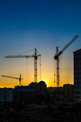 Big crane silhouette and many workers building new construction under a beautiful colorful sunset sky.Tall building under construction with scaffolds,Construction Site of New Building