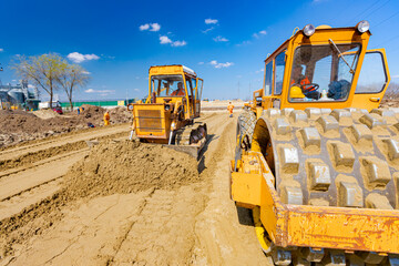 Road roller with spikes and earthmover are working at construction site